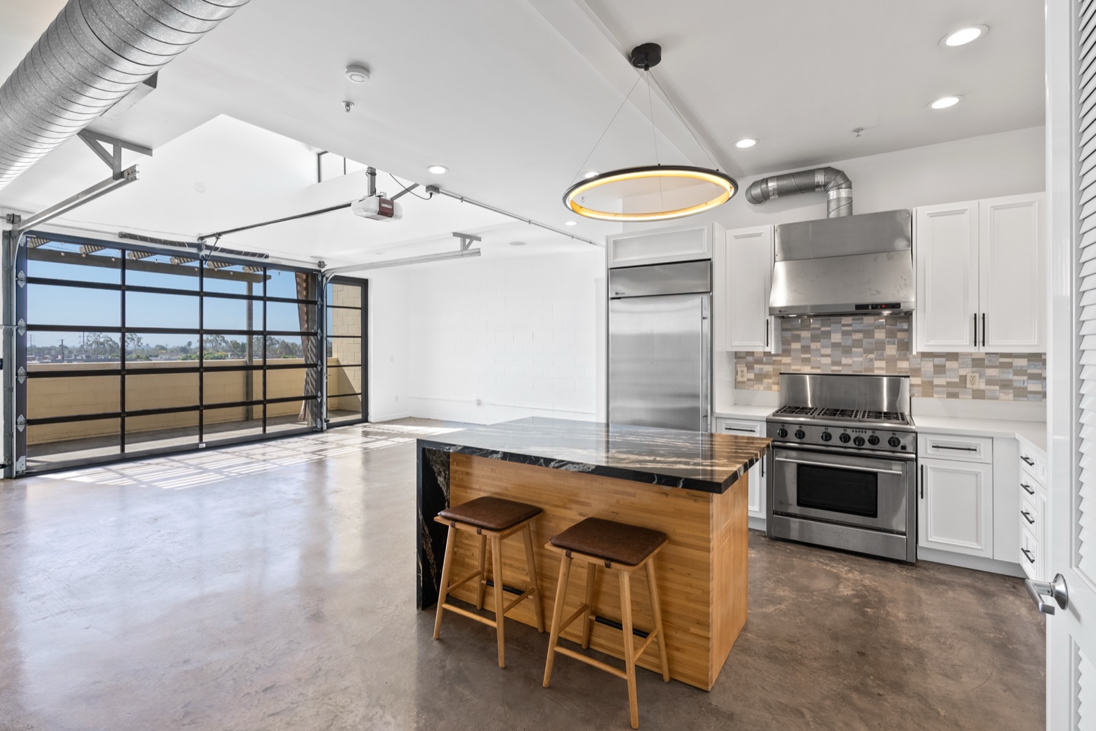 The kitchen and living room of 1544 12th Street #303 in Santa Monica, with polished concrete floors and a full-width glass roll-up wall to the terrace