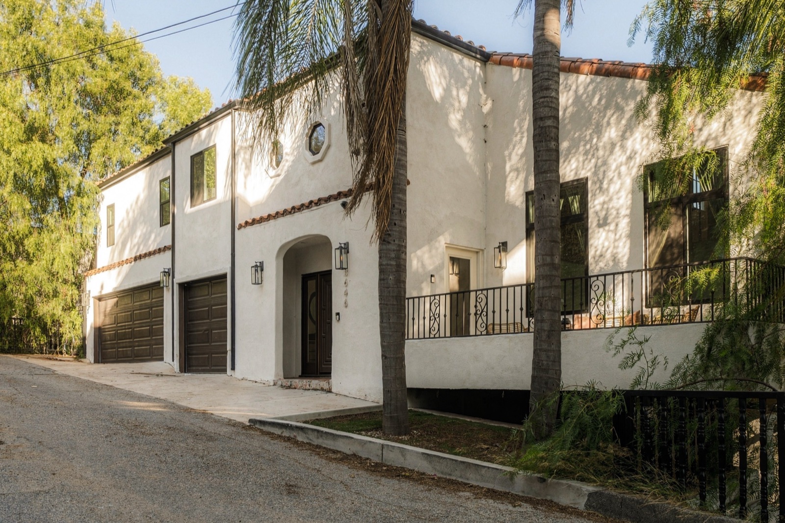 The street front of 3646 Potosi Avenue in Studio City, a white stucco Spanish Mediterranean home with a red tile roof framed by trees